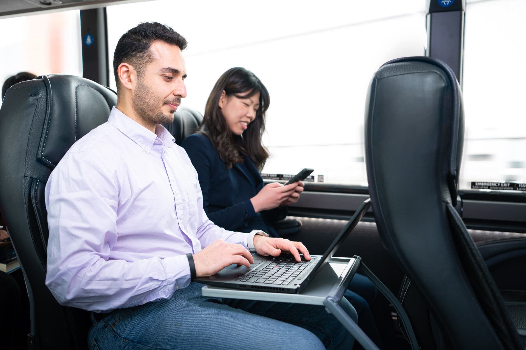 A passenger working on a laptop at his tray table on a Landline coach.